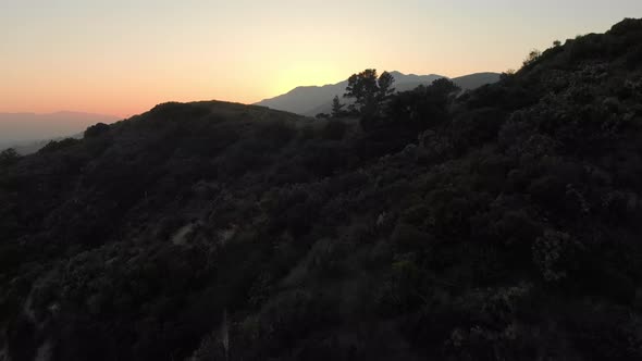 Aerial Low Pass Over Hill to Reveal Sunset Behind Mountain