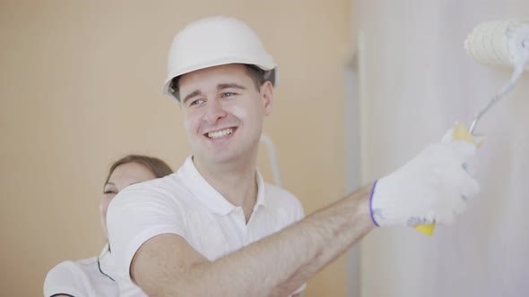 Young Man in Helmet is Painting a Wall with Paint Roller