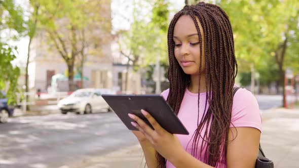 A Young Black Woman Works on a Tablet and Celebrates in the Street in an Urban Area