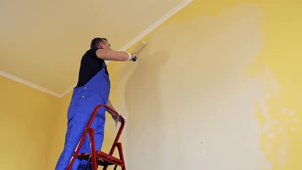 Man painting a yellow wall with a roller at work