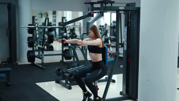 Girl in a black top and leggings performs an exercise on his chest simulator in a fitness club.