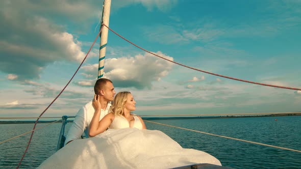 The Bride and Groom Are Sitting on a Yacht. Looking Into the Distance at Sunset. Beautiful Landscape