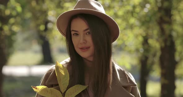 Portrait of Cute Caucasian Girl in Brown Hat in Autumn Park Looking at Camera and Smiling. Pretty