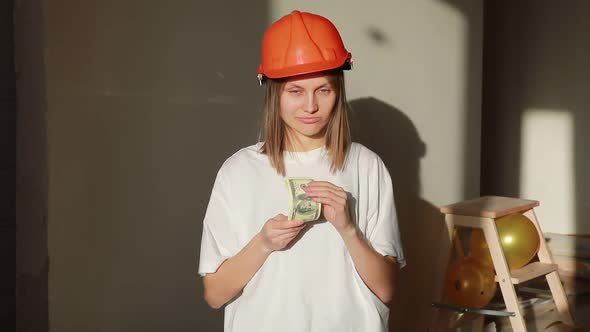 Young smiling female worker in orange hardhat and money hides in the bosom, standing at construction