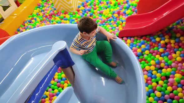 A Cheerful Preschooler Boy Descends From a Blue Slide Into the Pool with Balls in the Playroom