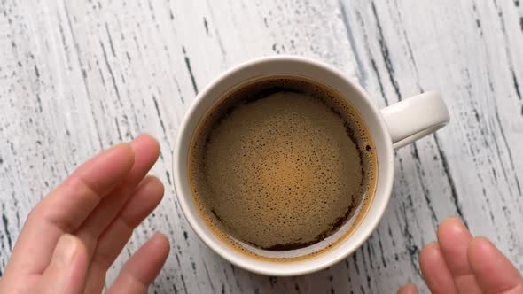 Female Hands Takes a Cup of Coffee. Woman Warms Her Hands with Hot Coffee Cup. Zoom Out Shot