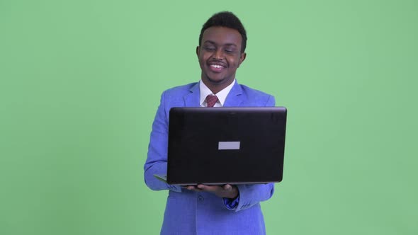Happy Young African Businessman Thinking While Using Laptop
