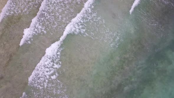 Aerial bird's eye view rising up above the shallow waters and waves along the shores of Cebu in the