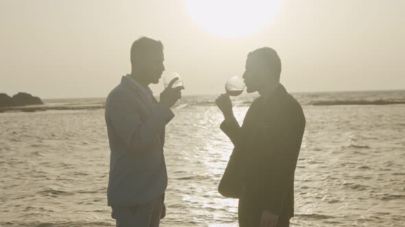 Gay couple drinking red wine on the beach during sunset