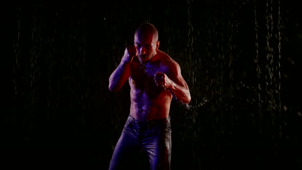 a Muscular Man with a Bare Torso Strikes with Hands in Streams of Water on a Dark Background