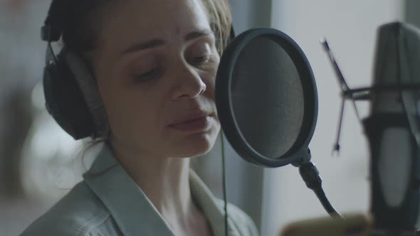 A Young Girl in Monitor Headphones in Front of a Microphone Records a Podcast