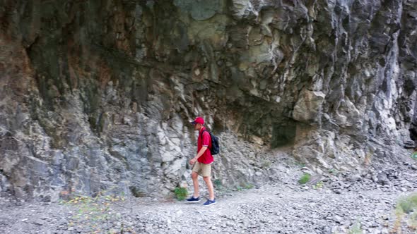 Man hiking in the mountains. Caucasian in red shirt and hat with a backpack walking alone on a trail