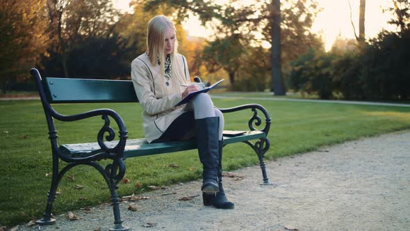 Beautiful Young Woman Is Writing a Diary Outdoors in the Park.