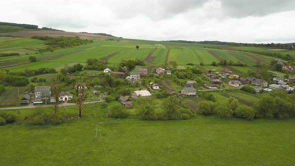 Aerial view of small village with small houses among green trees with farm fields and distant 