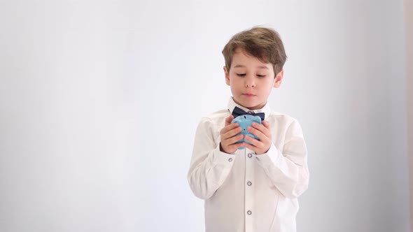 Asian Little Boy in a White Shirt with a Bow Tie Shakes an Empty Piggy Bank No Money Concept