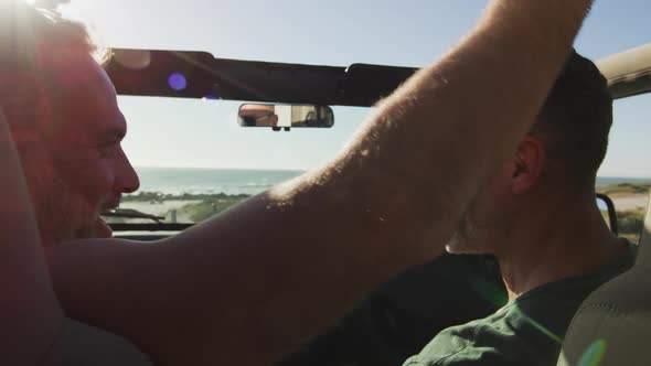 Happy caucasian gay male couple sitting in car and embracing on sunny day at the beach