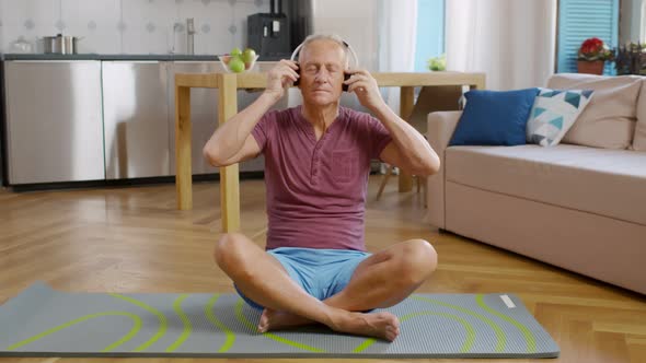 Senior Man in Headphones Meditating on Mat in Living Room