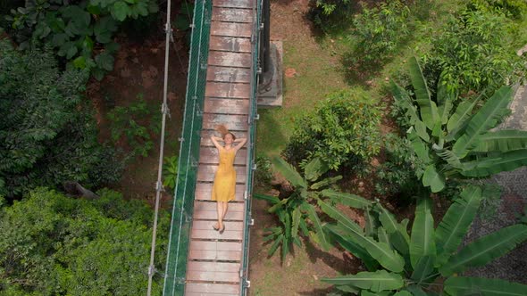 Aerial Shot of a Young Woman Lays on a Suspension Bridge Over the Jungles. Travel To South East Asia