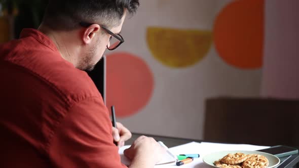 Man working in home office at table with laptop computer and notebook