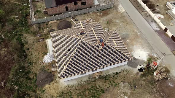 Aerial view of unfinished brick house with wooden roof frame structure under construction.