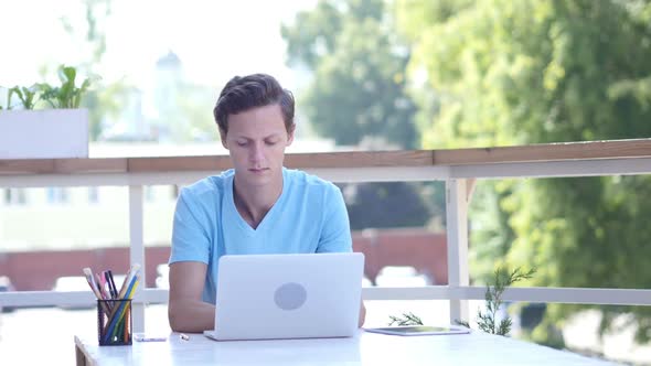 Young Man Working on Laptop, Sitting on Desk, Outdoor