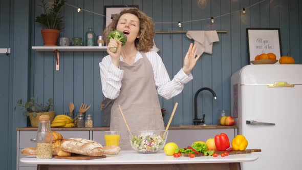 Young Woman Having Fun While Cooking And Singing In Broccoli On Kitchen