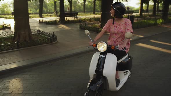 Young Beautiful Girl Riding Around City on Scooter at Sunrise