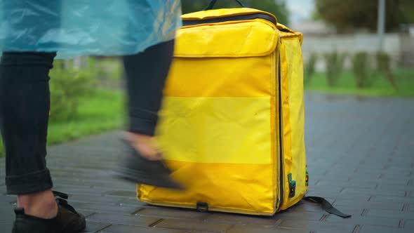 Unrecognizable Stressed Angry Courier Kicking Yellow Backpack Walking Away on Pavement Alley