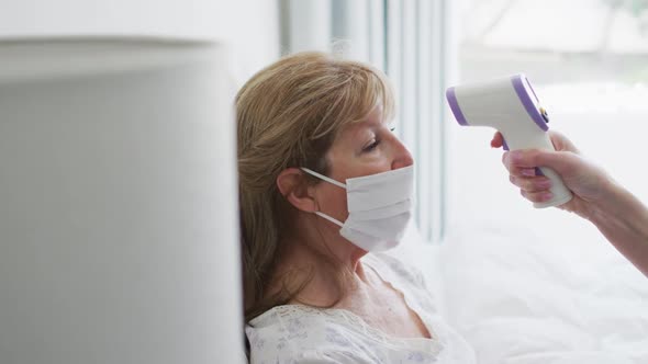 Senior woman wearing face mask getting her temperature measured at home