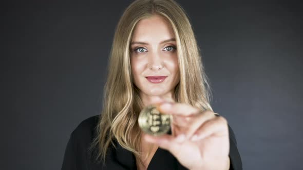 Young smiling blonde girl presenting a gold bitcoin coin to the camera.