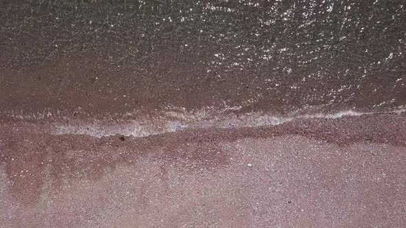 Aerial bird's eye view of shimmering waves lapping onto a pebble beach, STATIC CROP