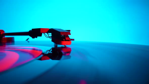 Black Vinyl Record Spinning and Play Music on Old Turntable in Rays of Bright Red and Blue Neon