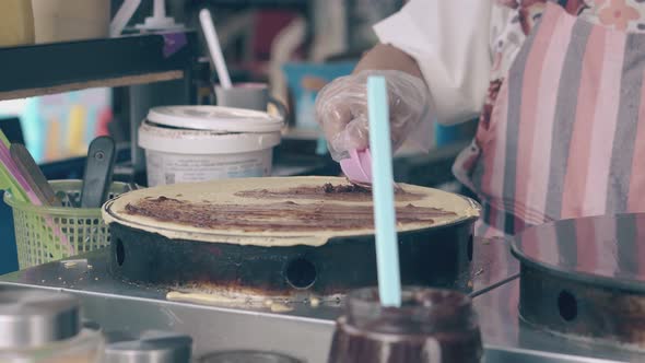 Woman Covers Pancake with Chocolate on Crepe Maker in Cafe