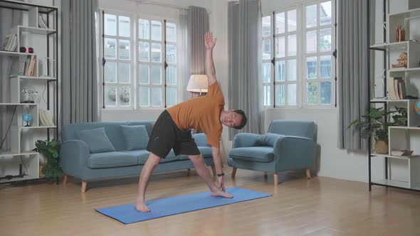 Asian Man Doing Yoga In Triangle Pose On Mat At Home