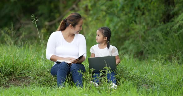 Mom reading a book and daughter using laptop