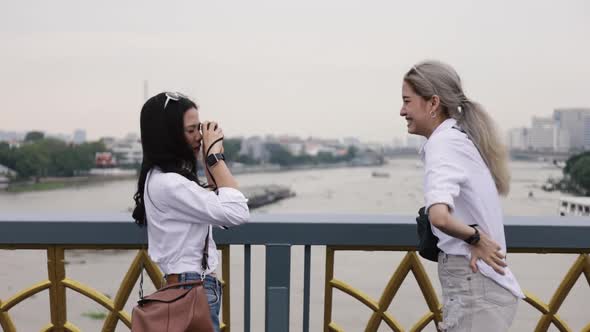 Happy Asian lesbian couple taking a photo while standing on the bridge.