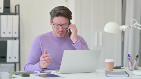 Angry Middle Aged Man with Laptop Talking on Smartphone 