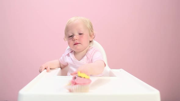 Baby girl sitting in highchair eating cupcake