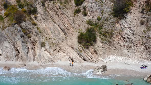 Aerial view of couple taking a stroll at seashore against huge cliffs on an isolated beach.