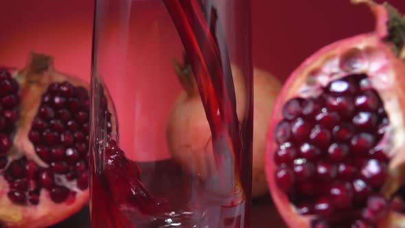 Closeup of Juice Flowing Into a Jug on the Red Background of Pomegranate Halves