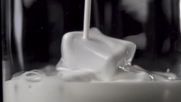 Milk is pouring on ice cubes in a glass on a dark background