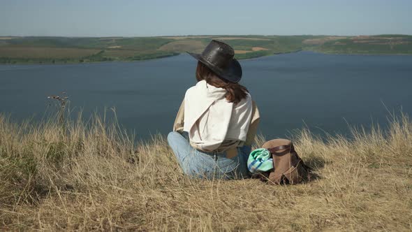 Young Woman in Cowboy Hat Sitting on Edge of Mountain