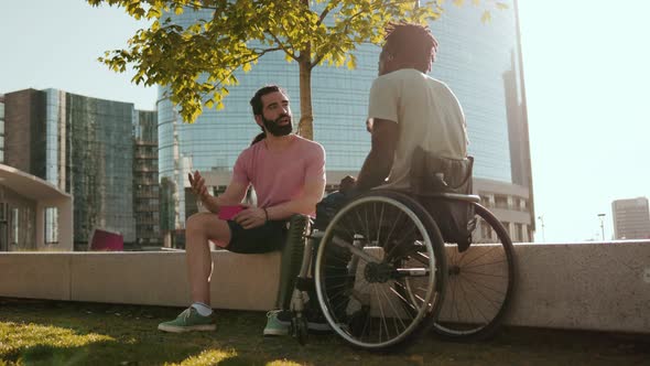 People with disability having fun outdoor - Man sitting on wheelchair talking to man with leg prosth