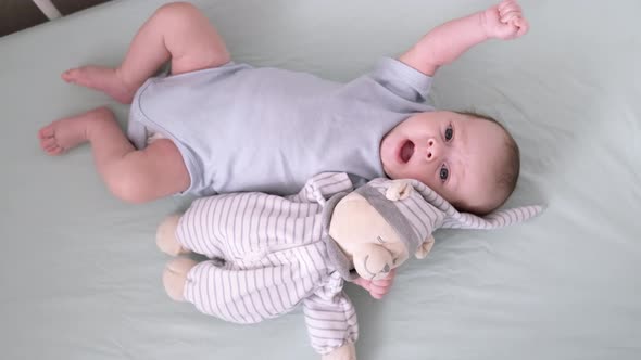 Newborn Baby Boy 3 Months Old Lies in Crib Nursery with Blue Clothes on His Back with Teddy Bear