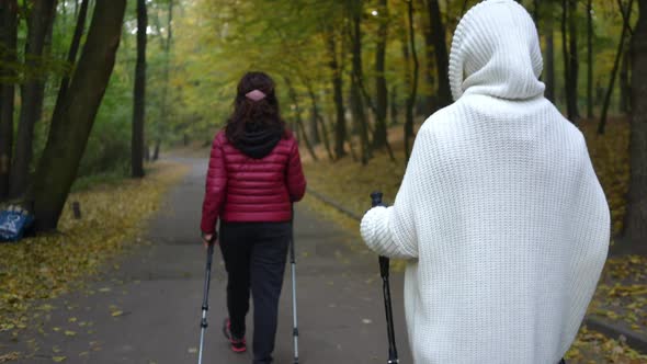 Back View Woman with Poles for Nordic Walking Following Friend Strolling at Front