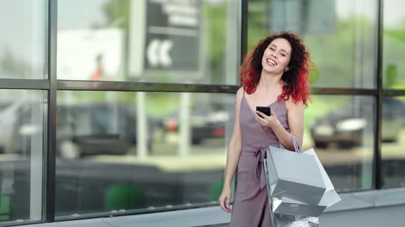 Charming Smiling Redhead Girl with Smartphone Enjoying Buying Walking Mall Glass Background