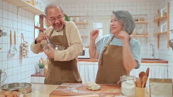 Asian Senior elderly Couple dancing together with happiness while cooking foods in kitchen at home.