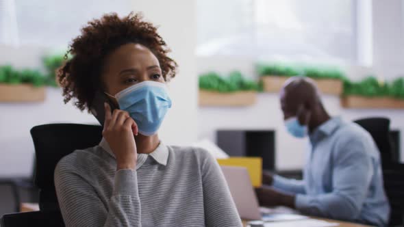 Diverse male and female business colleagues in face masks, woman talking on smartphone in office