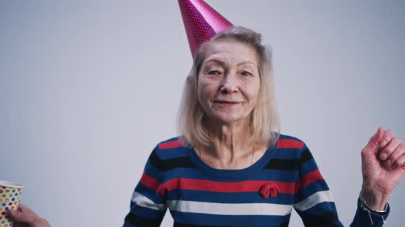 Happy Elderly Woman with Party Hat and Cup of Drink Dancing Indoors