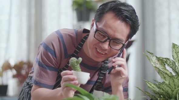 Close Up Of Asian Man With Plants Talking On Phone At Home